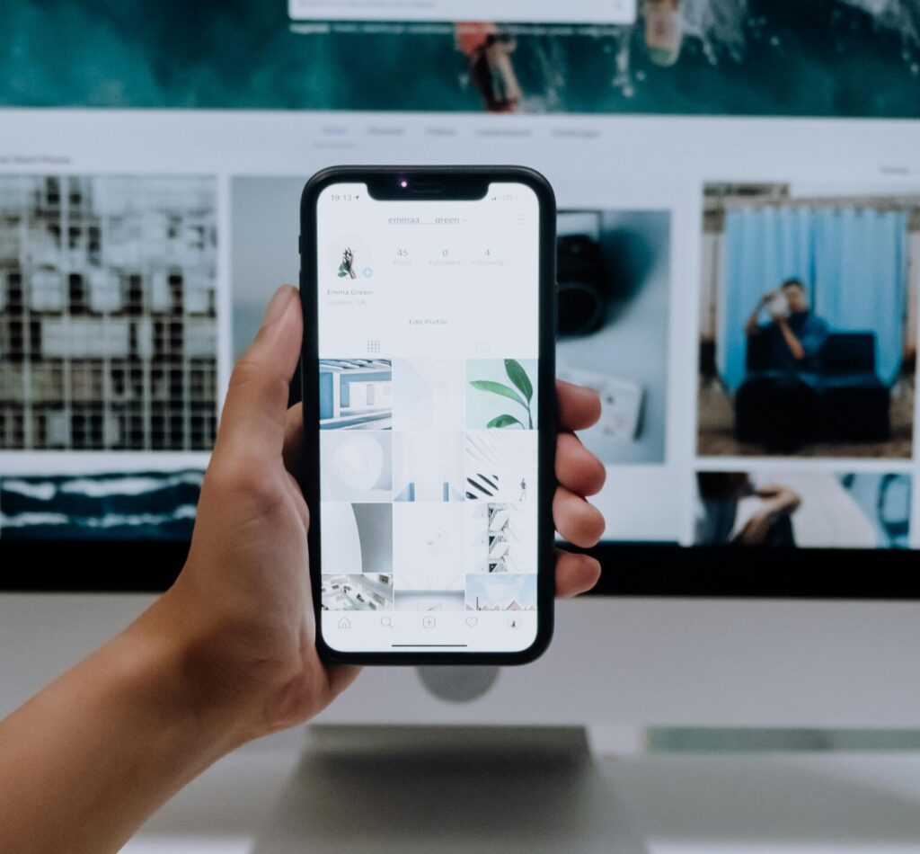 Person uses a smartphone in front of a computer screen displaying stock photos, showcasing modern technology use.